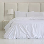 Cama vestida con funda nórdica blanca lisa de algodón egipcio de 300 hilos y fundas de almohada coordinadas.
