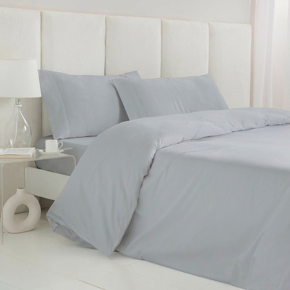 Funda nórdica de satén algodón egipcio GRIS PERLA de 300 hilos extendida sobre cama con almohadas a juego.