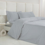 Funda nórdica de satén algodón egipcio GRIS PERLA de 300 hilos extendida sobre cama con almohadas a juego.