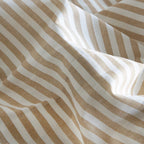 Sábana de algodón beige y mostaza sobre cama de matrimonio en ambiente sereno con decoración minimalista y tonos cálidos. A RAYAS
