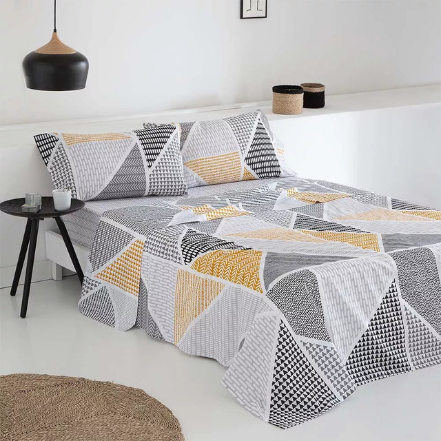 Juego de sábanas de poliéster y algodón compuesto por sábana encimera, bajera ajustable y funda de almohada, con tejido suave, resistente, transpirable y de fácil mantenimiento, presentado sobre una cama de estilo contemporáneo.